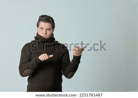 a man in a brown sweater and a bright color points to something and perfectly, showing an empty space with his thumb, shows everything on a light background, copy space