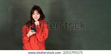 Banner of happy woman feeling happiness and standing typing smartphone on green background. Cute girl smiling wearing casual hoodie and connect internet shopping online and surfing. High quality photo