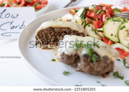 Low carb dinner or lunch with a mediterranean burger or meat ball. Served with a marinated zucchini, bell pepper, tomato salad on a plate. closeup and front view