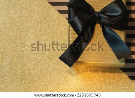 Gift box  with a black bow on sparkling golden wrapping paper.