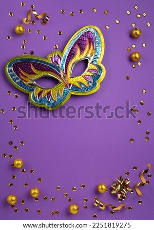 Mardi Gras masquerade festival carnival mask, sweet chocolate candies, gold beads and golden confetti on purple background. Holiday party invitation, greeting card concept.