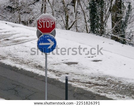 Stop and blue mandatory direction sign on a metal pole covered in snow