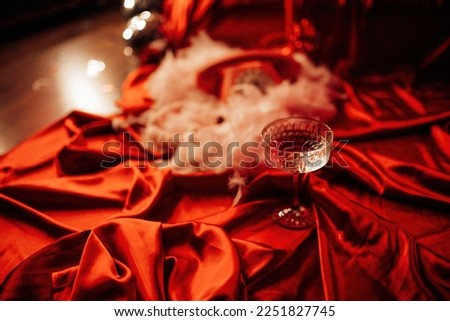 Extravagant glamour background with coupe glass of sparkly wine for love party at muffled light. Beautiful romantic burlesque place for st valentines holiday in red silk glossy sheets Royalty-Free Stock Photo #2251827745