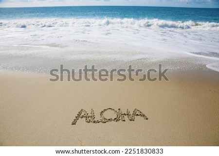 Aloha. The Word ALOHA written in the sand on the beach in Hawaii. Aloha tropical vacation message handwritten on a smooth sand beach with incoming wave 
Aloha Hawaii beach. 