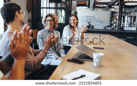 Happy business people applauding during a meeting in an office. Business colleagues celebrating success in a boardroom. Team of professionals working together in a startup. Royalty-Free Stock Photo #2251834601