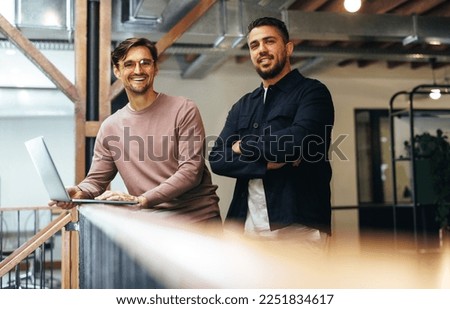Male business professionals standing on an interior balcony and looking at the camera. Two business men working together in a tech startup. Royalty-Free Stock Photo #2251834617