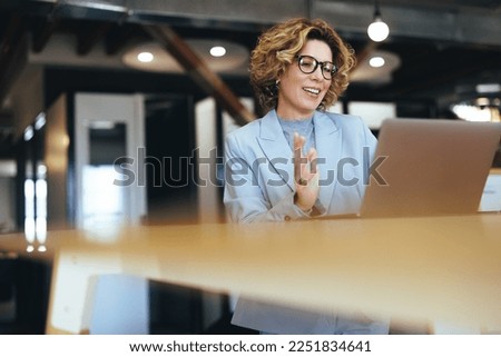Business woman waving on a video call in a coworking office. Caucasian business woman having an online meeting with her team. Professional woman doing remote work with a laptop. Royalty-Free Stock Photo #2251834641