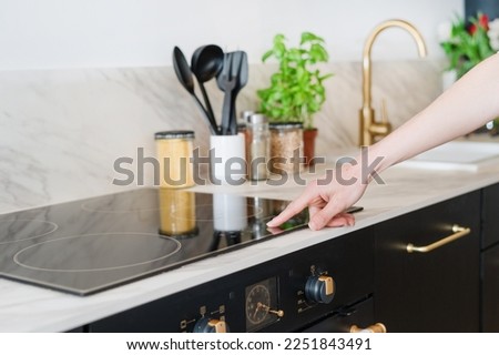 cropped shot of female hand press sensor button and using electrical hob for cooking dinner at home kitchen with stylish interior, modern household appliances concept Royalty-Free Stock Photo #2251843491