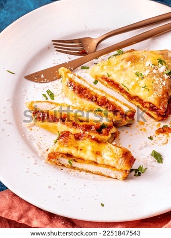 Chicken Parm, sliced and served on a white table with copper utensils, served with mozzarella cheese, parmesan cheese and tomato sauce Royalty-Free Stock Photo #2251847543