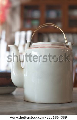 white ceramic teapot There was white smoke from the heat of the water coming out of the mouth of the tea kettle, placed on the cream marble table. Behind it is a teapot. Far and blurry
