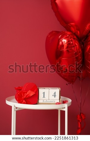 Calendar with date 14 FEBRUARY, candles and gift on table in room