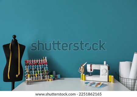 Tailor's workplace with sewing machine, threads and mannequin near blue wall Royalty-Free Stock Photo #2251862165