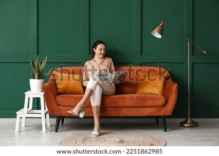 Young woman reading magazine on red sofa near green wall Royalty-Free Stock Photo #2251862985