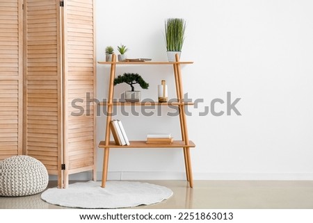 Interior of room with folding screen, shelving unit and pouf near white wall