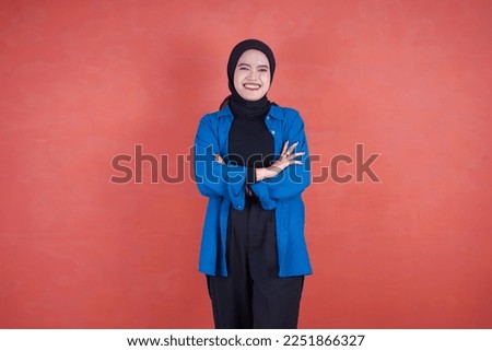 Beautiful Asian woman in blue shirt and hijab smiling cheerfully on brown background