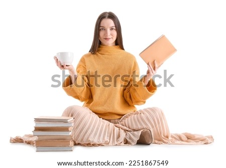 Young woman with cup of cocoa and books sitting on white background
