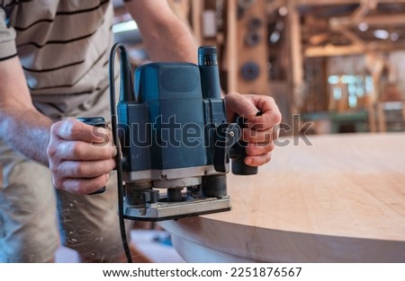 male carpenter working with hand-held power tools on a wooden table  Royalty-Free Stock Photo #2251876567