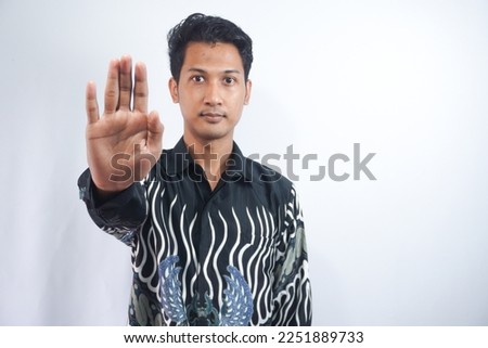 Portrait of serious young Asian man showing stop gesture, demonstrating denial sign, rejecting something unwanted isolated on white background