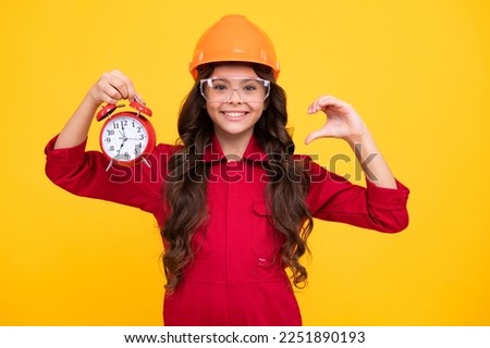 Excited teenager girl in builder helmet and clock alarm. Time to renovation and repair. Child in hard hat. Kid builder painter on construction site.