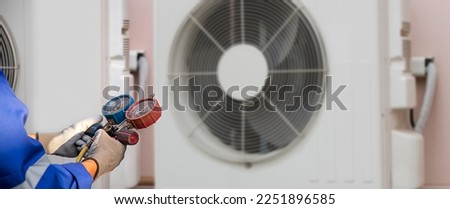 Heat and Air Conditioning, HVAC system service technician using measuring manifold gauge checking refrigerant and filling industrial air conditioner after duct cleaning maintenance outdoor compressor. Royalty-Free Stock Photo #2251896585