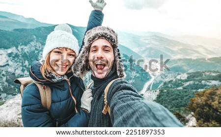 Happy couple of hikers taking selfie picture on top of the mountain - Two travelers with backpack smiling together at camera - Travel blogger influencer streaming using smart mobile phone device 