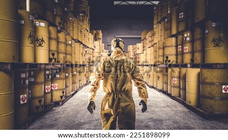 Man in yellow protective suit and gas mask, warehouse full of yellow metal barrels with danger symbols. Royalty-Free Stock Photo #2251898099