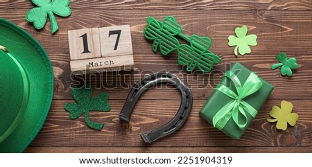 Calendar with date MARCH, 17, symbols of St. Patrick's Day and gift on wooden background