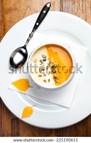 Pumpkin soup with cream and pumpkin seeds in a white bowl on wooden table
