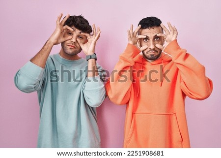 Young hispanic gay couple standing over pink background trying to open eyes with fingers, sleepy and tired for morning fatigue 