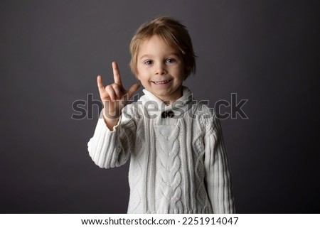 Cute little toddler boy, showing I LOVE YOU gesture in sign language on gray background, isolated image, child showing hand sings for deaf people