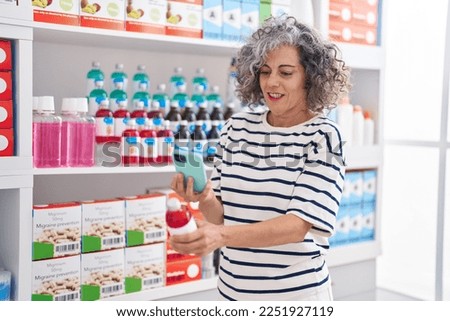 Middle age grey-haired woman client make photo to medication bottle by smartphone at pharmacy