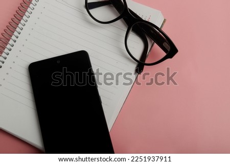 top view of cellular phone glasses and agenda on pink background with copy space