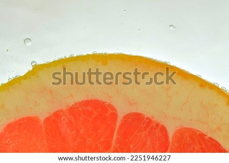 Close-up of fresh grapefruit slice on white background. Slice of red grapefruit in sparkling water on white background, close-up. Horizontal image.