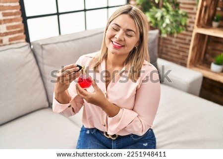 Young hispanic woman using perfume sitting on sofa at home