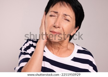 Senior woman suffering from ear pain on light grey background Royalty-Free Stock Photo #2251950929