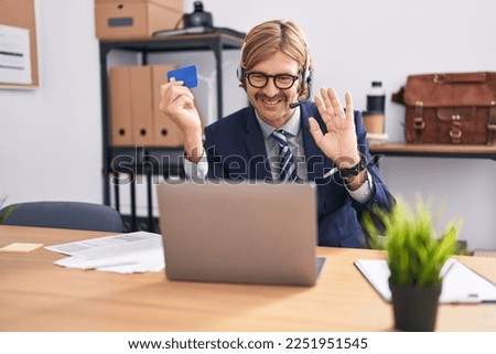 Caucasian man with mustache working at the office doing online shopping looking positive and happy standing and smiling with a confident smile showing teeth 