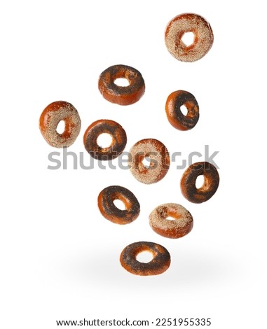 Many fresh bagels with poppy and sesame seeds falling on white background