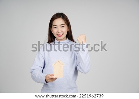 Portrait of smile happy excited Asian woman holding wood home for real estate concept loan buy and rent real estate such as houses, townhouses, townhomes and condos. Land Broker Business. 
