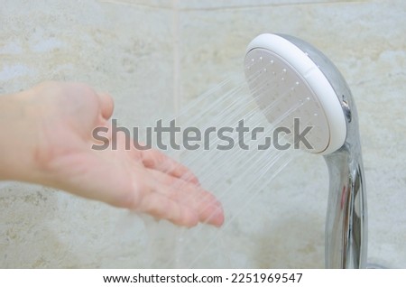 Female hand and water jet, focus on shower head. Hygiene procedures in the bathroom. Water for washing and cleansing the body. New plumbing and beige wall tiles.
