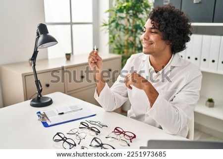 Young hispanic man optician holding eye drop at clinic
