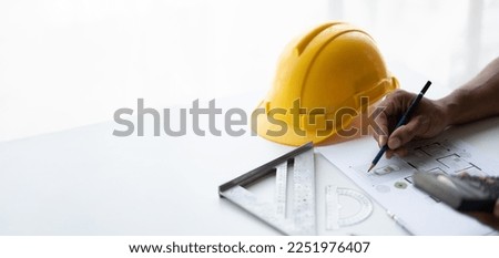 Engineer drawing a blue print design building or house, An engineer workplace with blueprints, pencil, protractor and safety helmet, Industry concept, copy space.