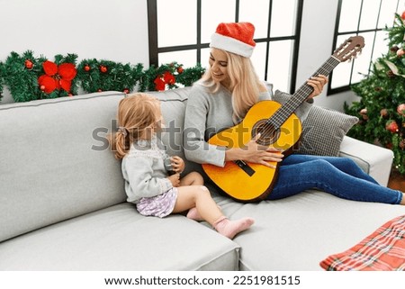 Mother and daughter playing guitar and singing sitting by christmas tree at home