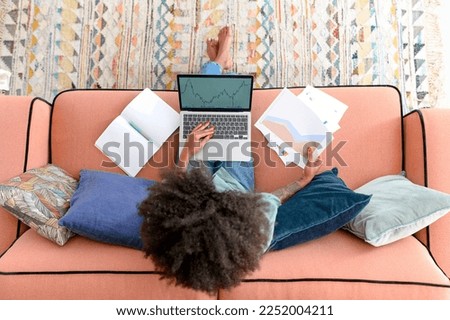 Overhead view of multiracial ethnic woman or female freelancer sitting on the couch and using laptop for remote work, doing paperwork, looking through documents. Modern home office concept Royalty-Free Stock Photo #2252004211