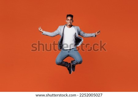 Full body young employee business man corporate lawyer wear formal grey suit shirt glasses work in office jump high hold spreading hands in yoga om aum gesture isolated on plain red orange background