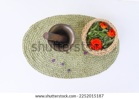 Medicinal herbs. Calendula and yarrow flowers. Copper mortar and plants in a jute basket on the wicker mat background.