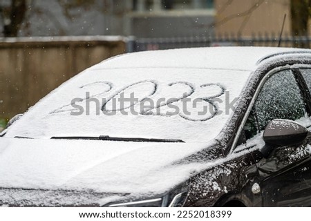 Windscreen wipers and a snow covered car, front view, 2023 inscription. handwritten on snowy window