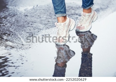 A young woman walks through the puddles in white sneakers and blue jeans on a spring, summer day. Separate parts of the body, legs, shoes. Concept for article, cover, website, healthy lifestyle.