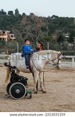 Wheelchair and boy with disability on horse in a physiotherapy session Royalty-Free Stock Photo #2252031359