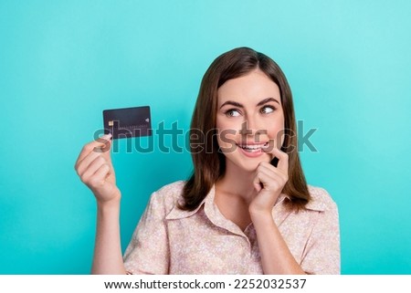 Photo of tricky cunning lady wear pink shirt biting finger looking bank card empty space isolated turquoise color background