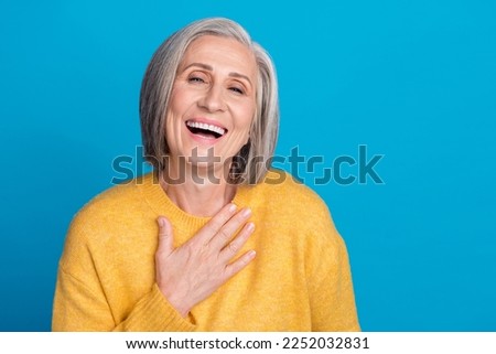 Photo portrait of mature lovely lady hands touch chest laughing have fun dressed stylish yellow outfit isolated on blue color background